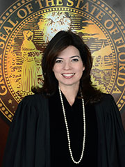 Portrait of a smiling judge in formal attire standing in front of the Florida State Seal engraved on a wall